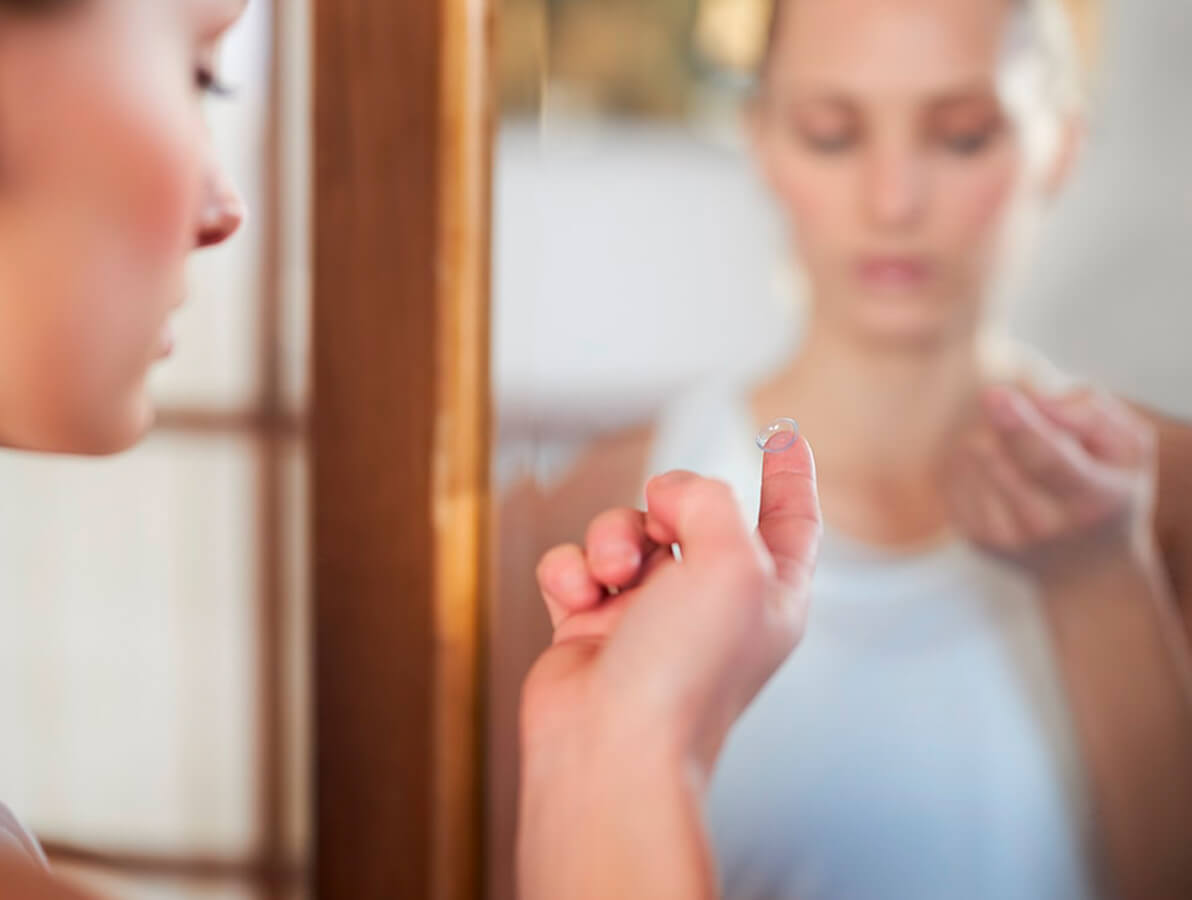 Kvinde foran spejlet, klar til at påføre en kontaktlinse.