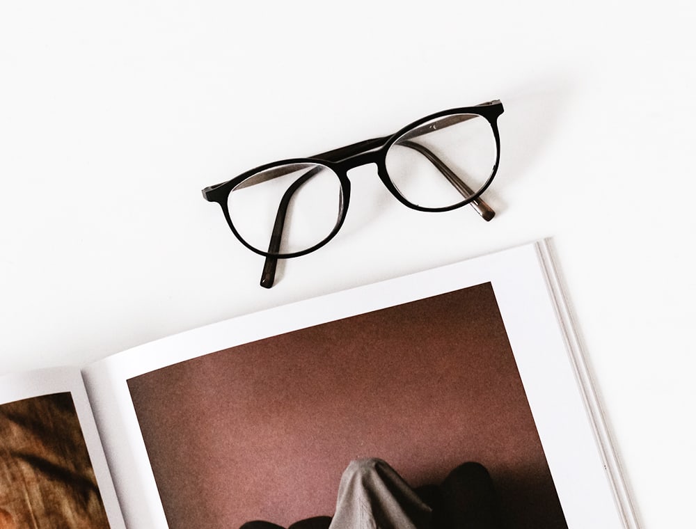 Vit bakgrunn med svarte brilleinnfatninger og en åpen bok med bilder.