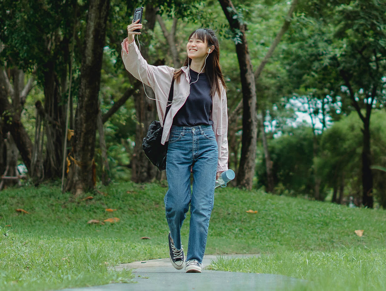 Kvinna promenerar i naturen och tar en bild av sig själv, smilende, med sin mobiltelefon.