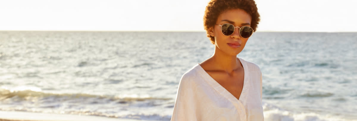 Kvinne med solbriller foran havet.