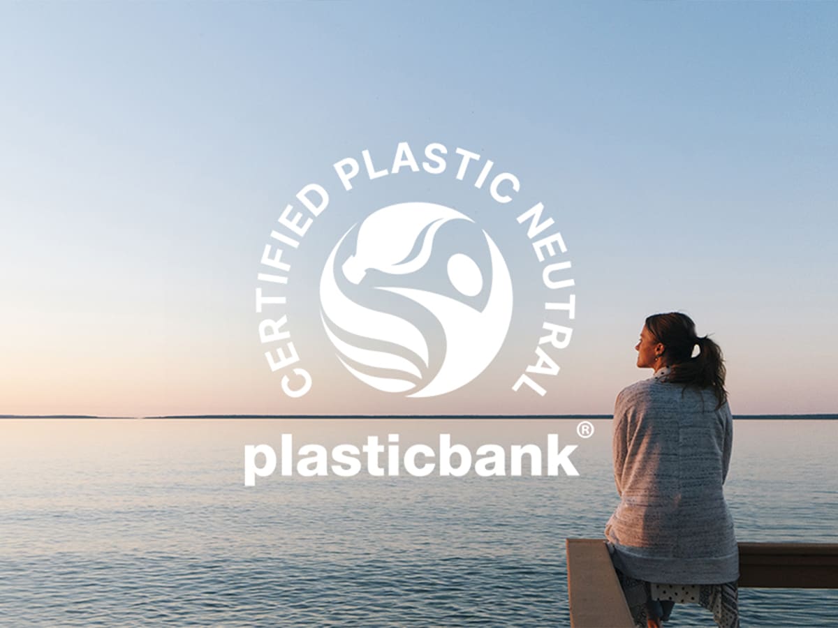 Kvinne sitter på en brygge og ser ut over vannet, med en tegnet logo over som sier: Certified plastic neutral plasticbank.