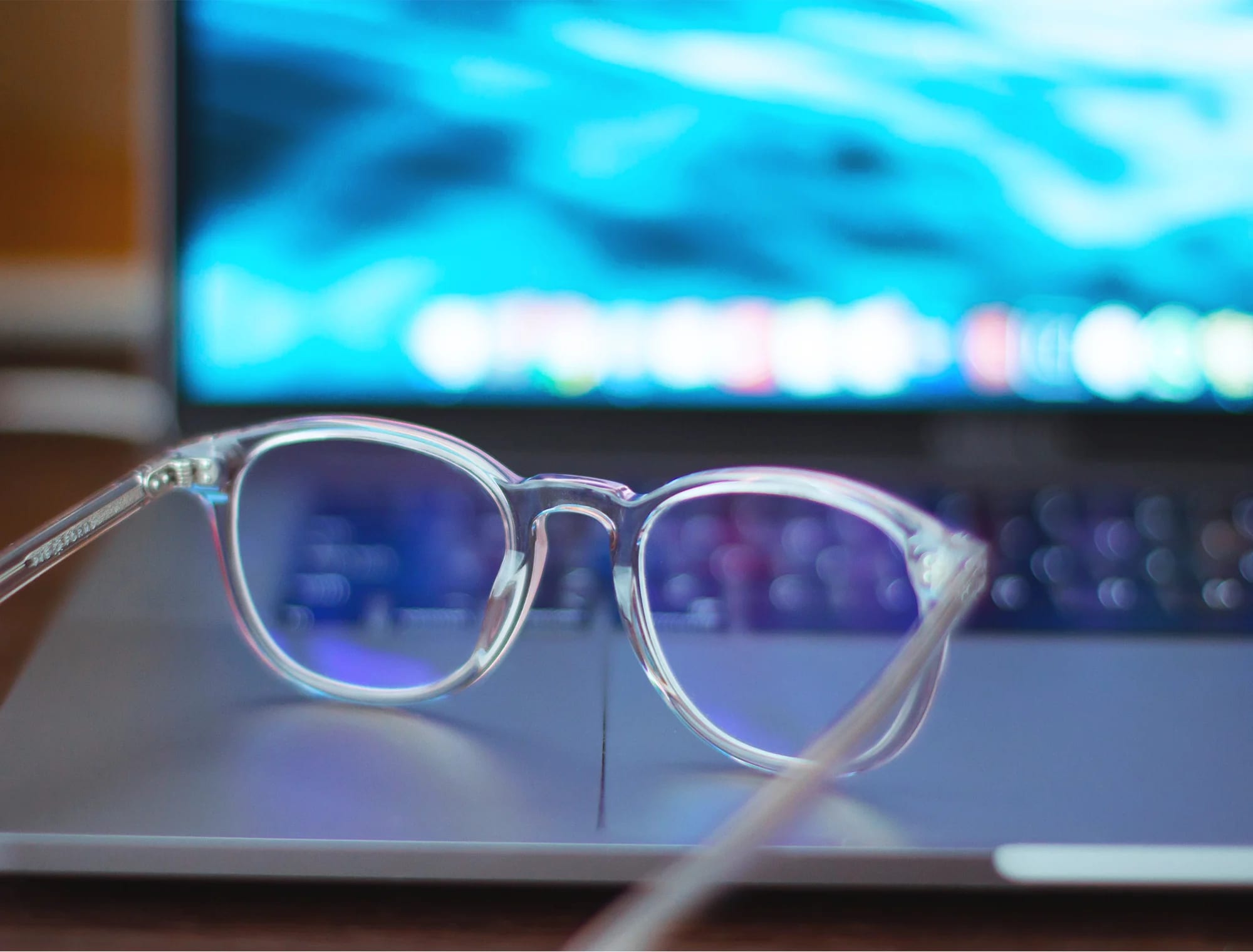 Läpinäkyvät silmälasit lepäävät kannettavan tietokoneen päällä sinisen valon loisteessa.