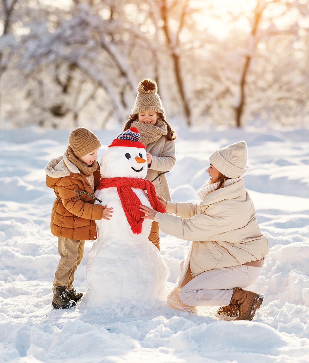 Bilde av en kvinne og to barn som bygger en snømann en solrik vinterdag.