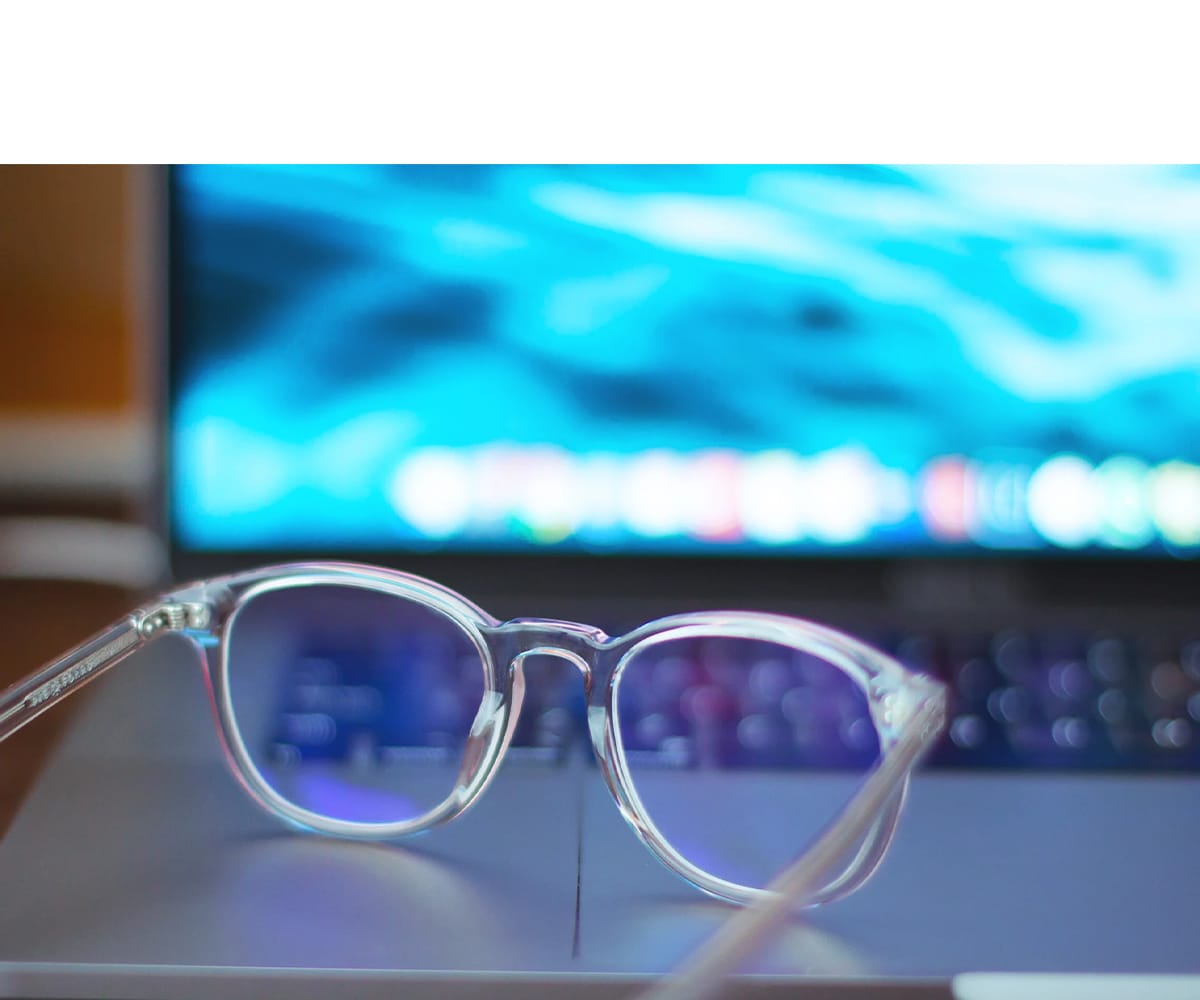 Gjennomsiktige briller på tastaturet til en bærbar datamaskin med blått lys.
