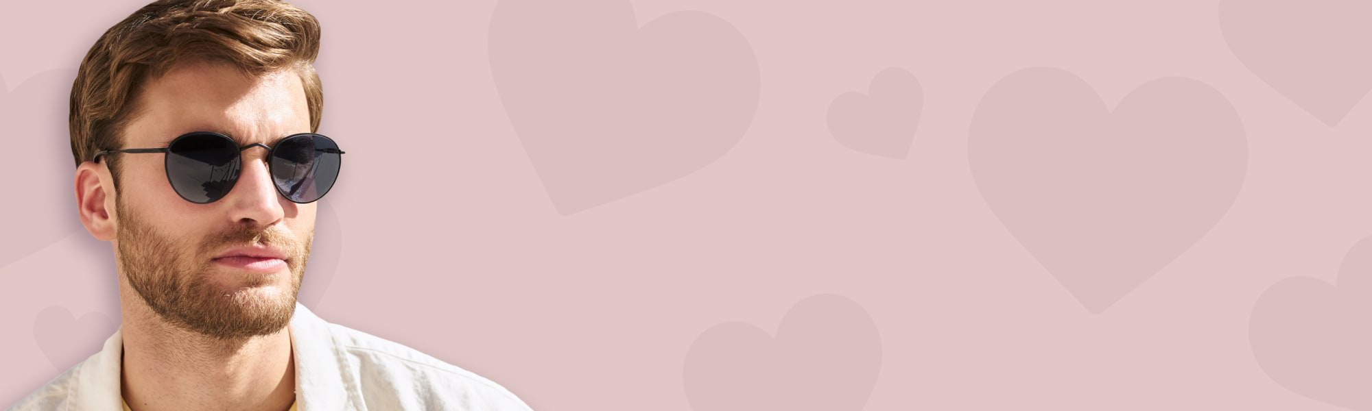 Manlig modell med svarta, runda solglasögon på en rosa bakgrund med hjärtan