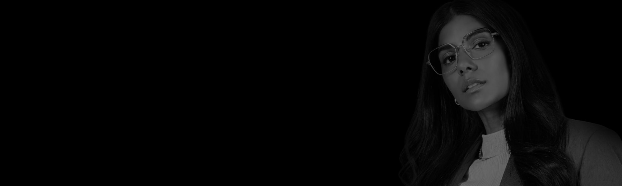 En kvinna med svart hår och stora metallbågar tittar åt sidan.