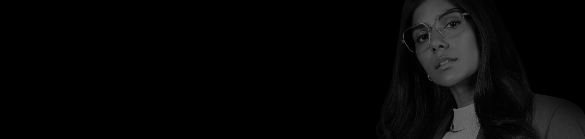 En kvinne med svart hår og store metallbriller ser til siden.