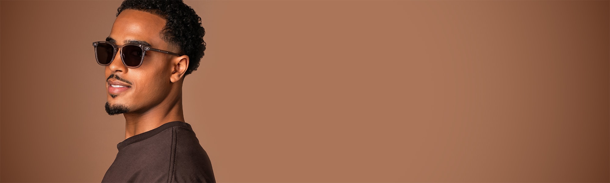 Banner som visar en man i mörka solglasögon med genomskinliga bågar mot en varmbrun bakgrund.