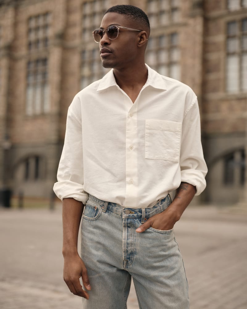 A man in Mareld CJ2411 sunglasses, wearing a white shirt tucked into light-washed jeans. He poses casually in front of an elegant historic building, exuding effortless style.