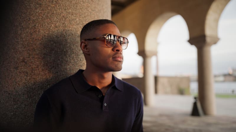 A man wearing brown sunglasses with a large classic shape, combined with a blue shirt.